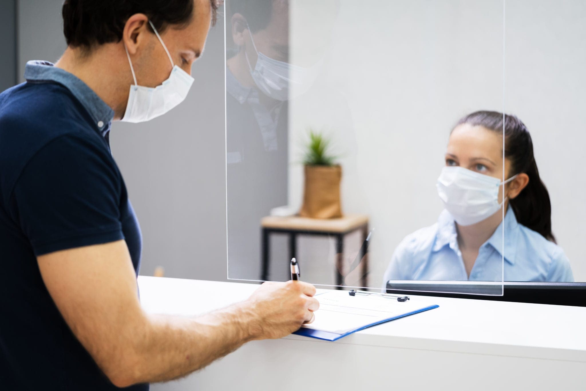 Client Signing Paper At Reception Desk In Face Mask