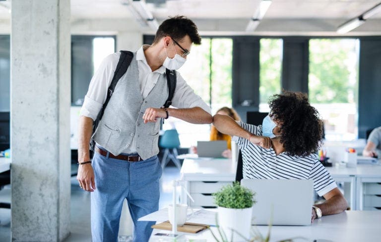 Two coworkers wearing face masks greeting with elbow bump in modern office