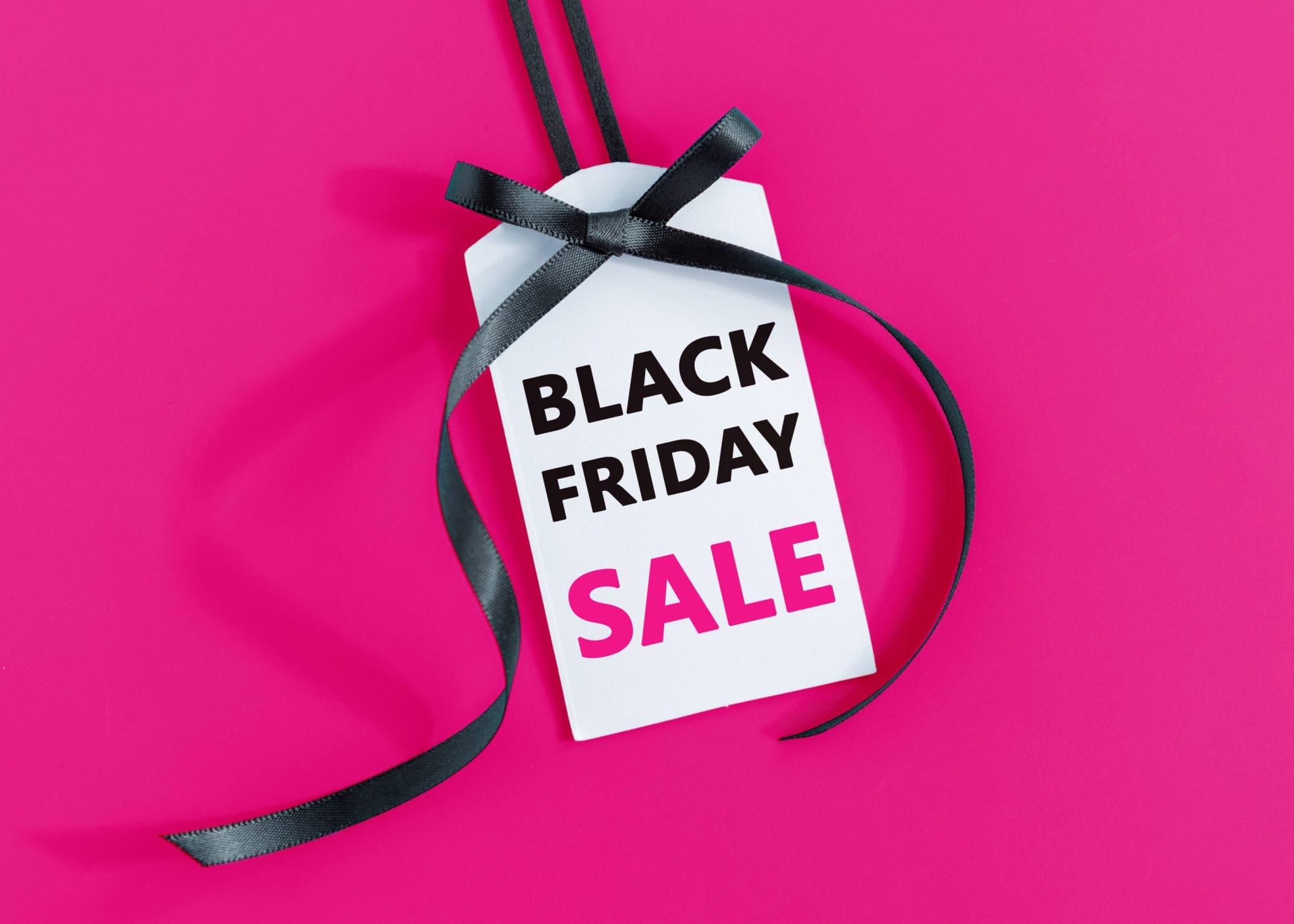 White sale tag with black ribbon on pink background displaying Black Friday Sale text