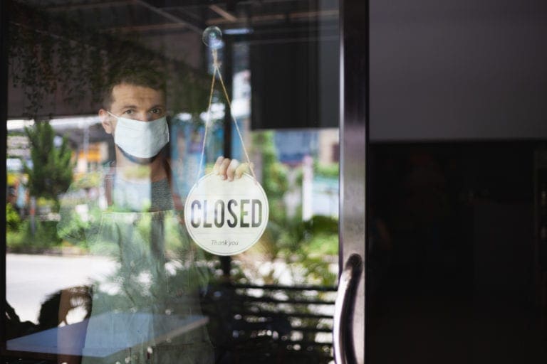 Shop owner wearing a face mask holding a "Closed" sign on the front door during lockdown