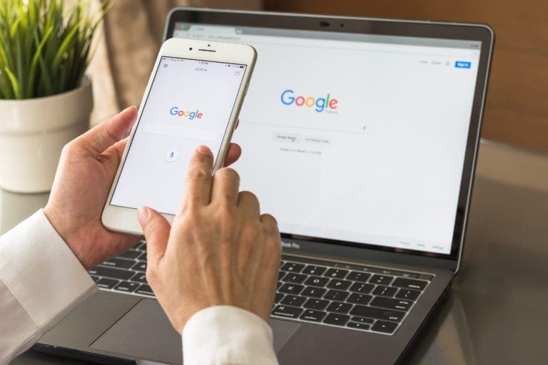 Person using Google Search on a smartphone and laptop at the same time.
