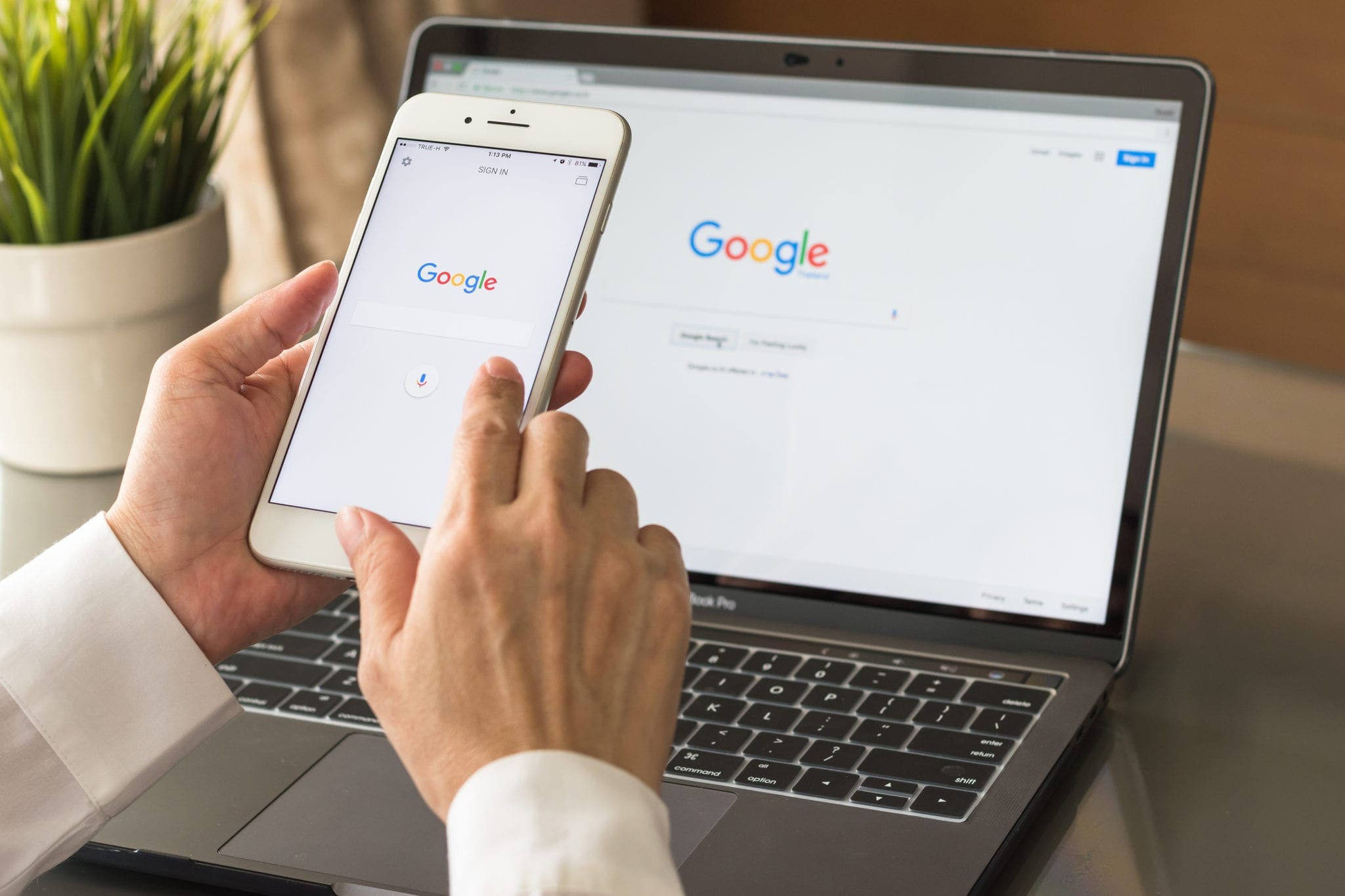 Person using Google Search on a smartphone and laptop at the same time.