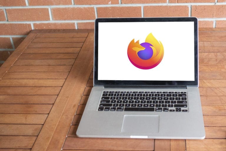 Laptop displaying the Firefox browser logo on a wooden table with a brick wall background.