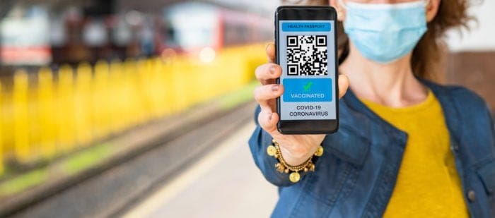 Woman holding smartphone displaying NHS COVID Pass at a train station