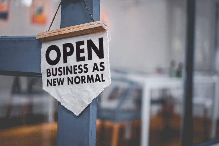 Open sign with “Business as New Normal” message on a shop door
