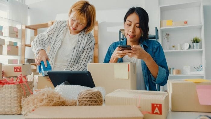 Two women preparing eCommerce orders with packaging materials and boxes