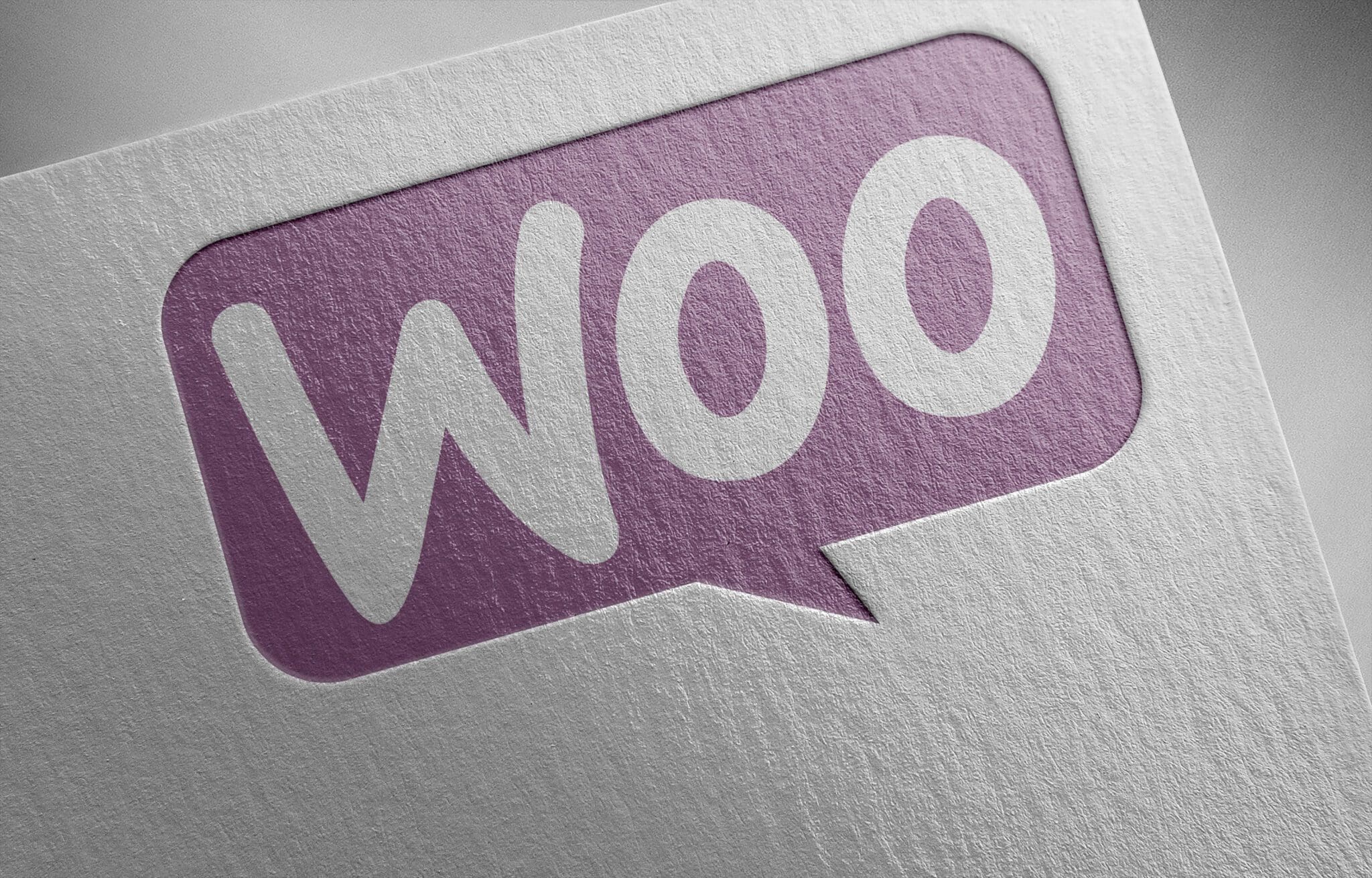 Close-up of embossed WooCommerce logo in purple speech bubble on white textured paper
