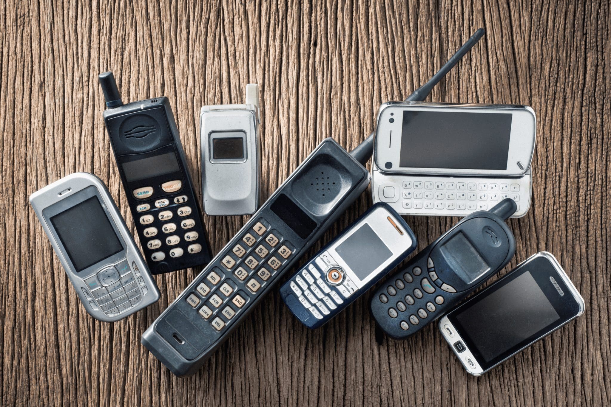 Collection of old mobile phones on wooden background, celebrating 50 years of mobile technology from the first call to modern devices.