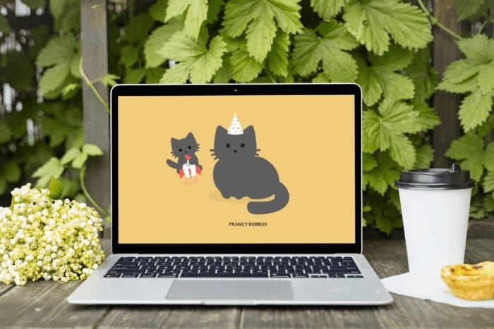 Laptop showing Tabby Cat browser extension with cute cartoon cats, placed on a wooden table outdoors with coffee cup, pastel de nata, and spring flowers