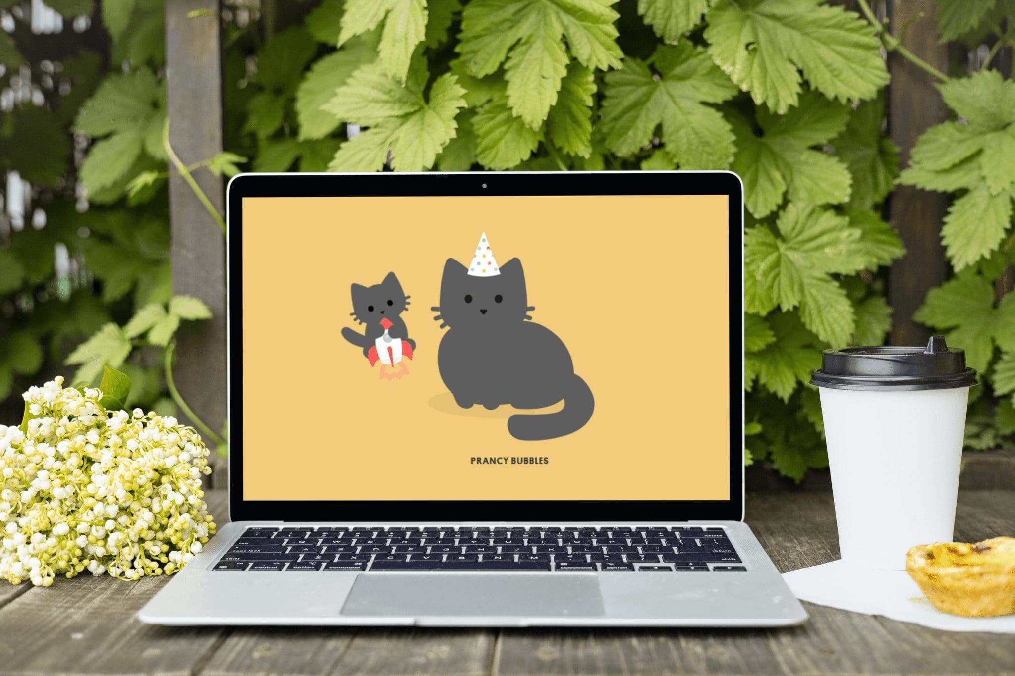 Laptop showing Tabby Cat browser extension with cute cartoon cats, placed on a wooden table outdoors with coffee cup, pastel de nata, and spring flowers