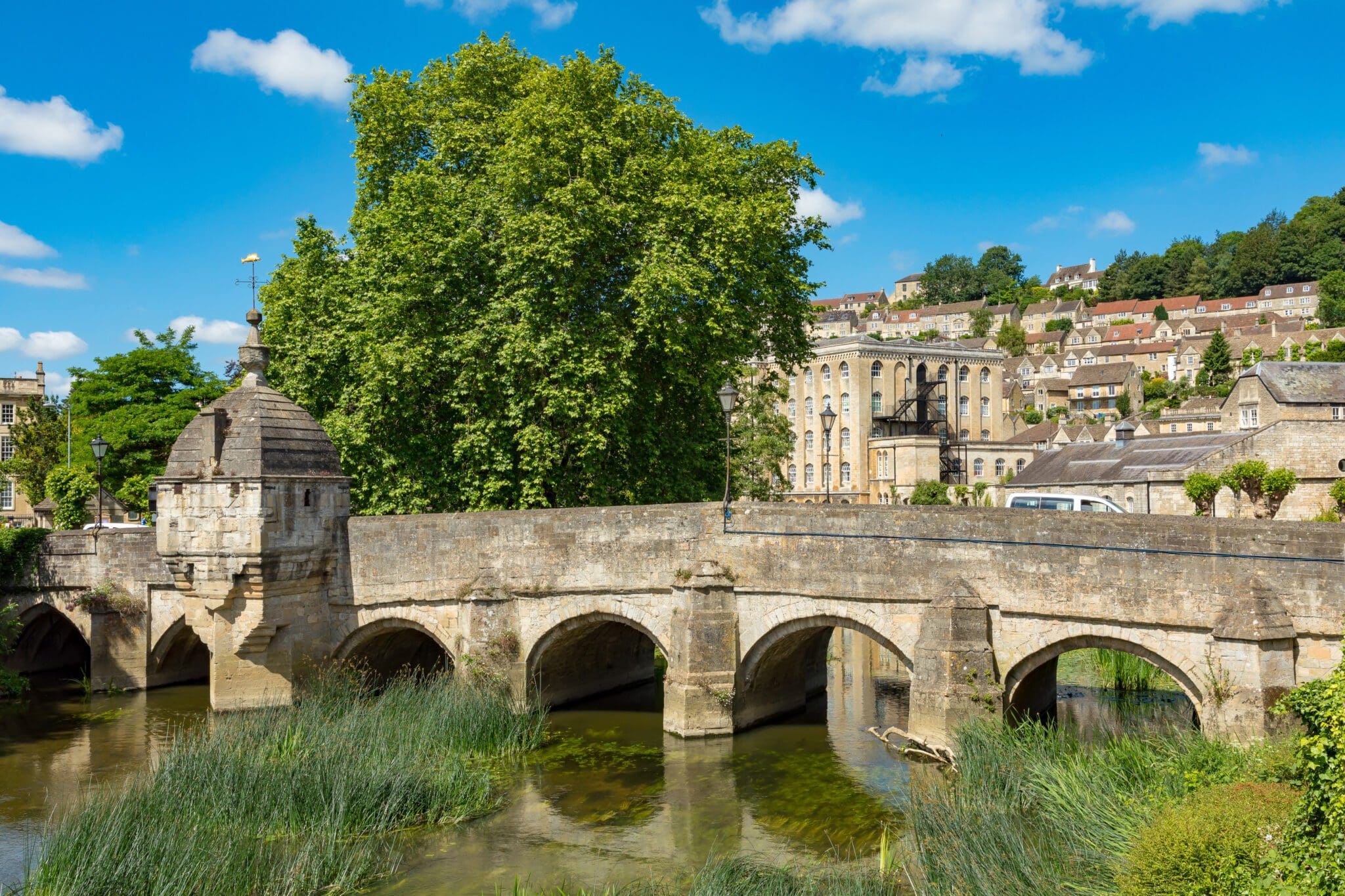 A scenic view of a historic stone bridge and lush green surroundings in Wiltshire on a sunny day.