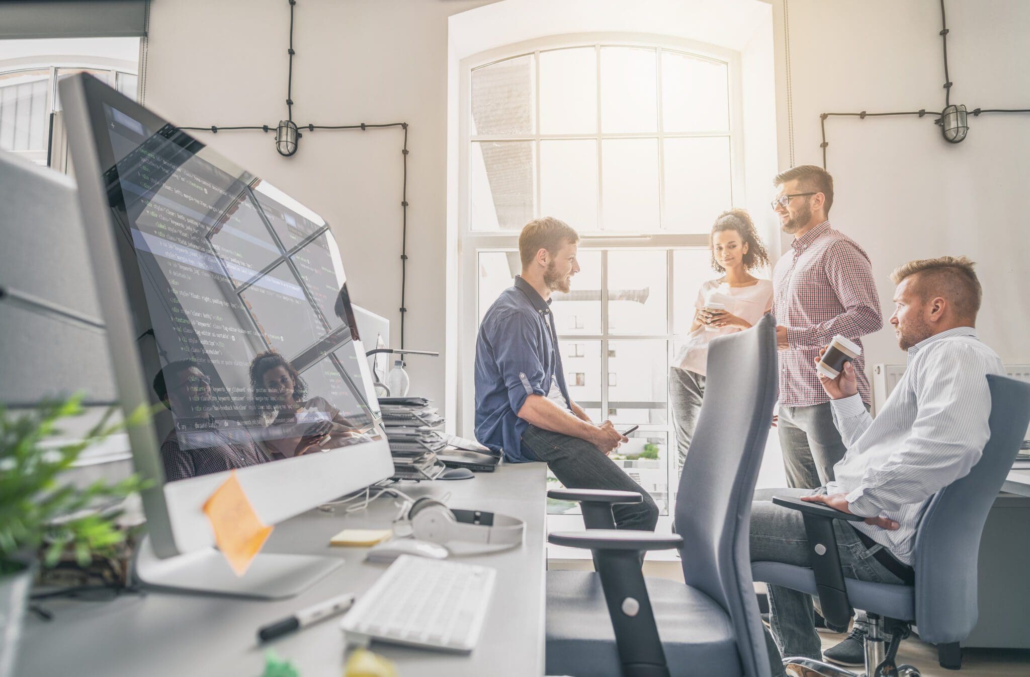 A team of professionals discussing web design and development, with coding visible on a monitor, highlighting collaboration in web design for small businesses.