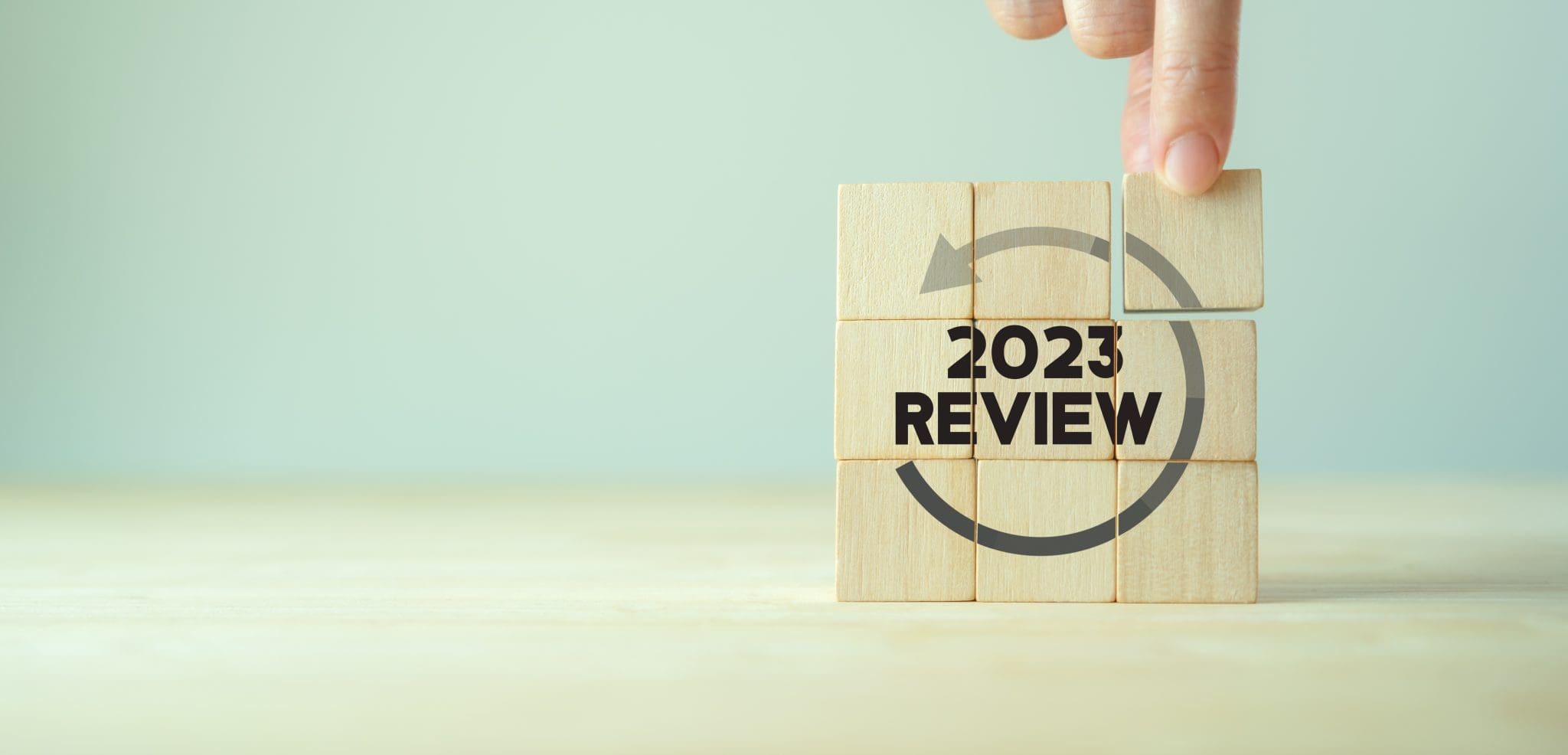 Hand placing a final wooden block on a cube with the text “2023 Review” and a circular arrow