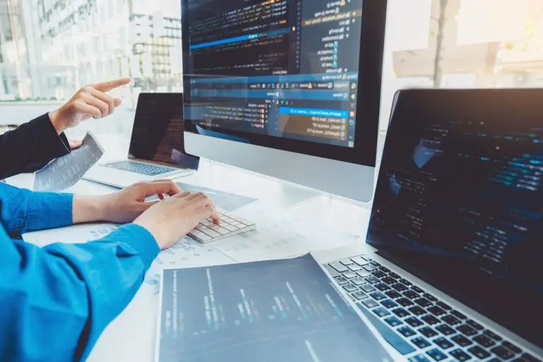 Developers collaborating on coding projects using multiple screens and printed flowcharts