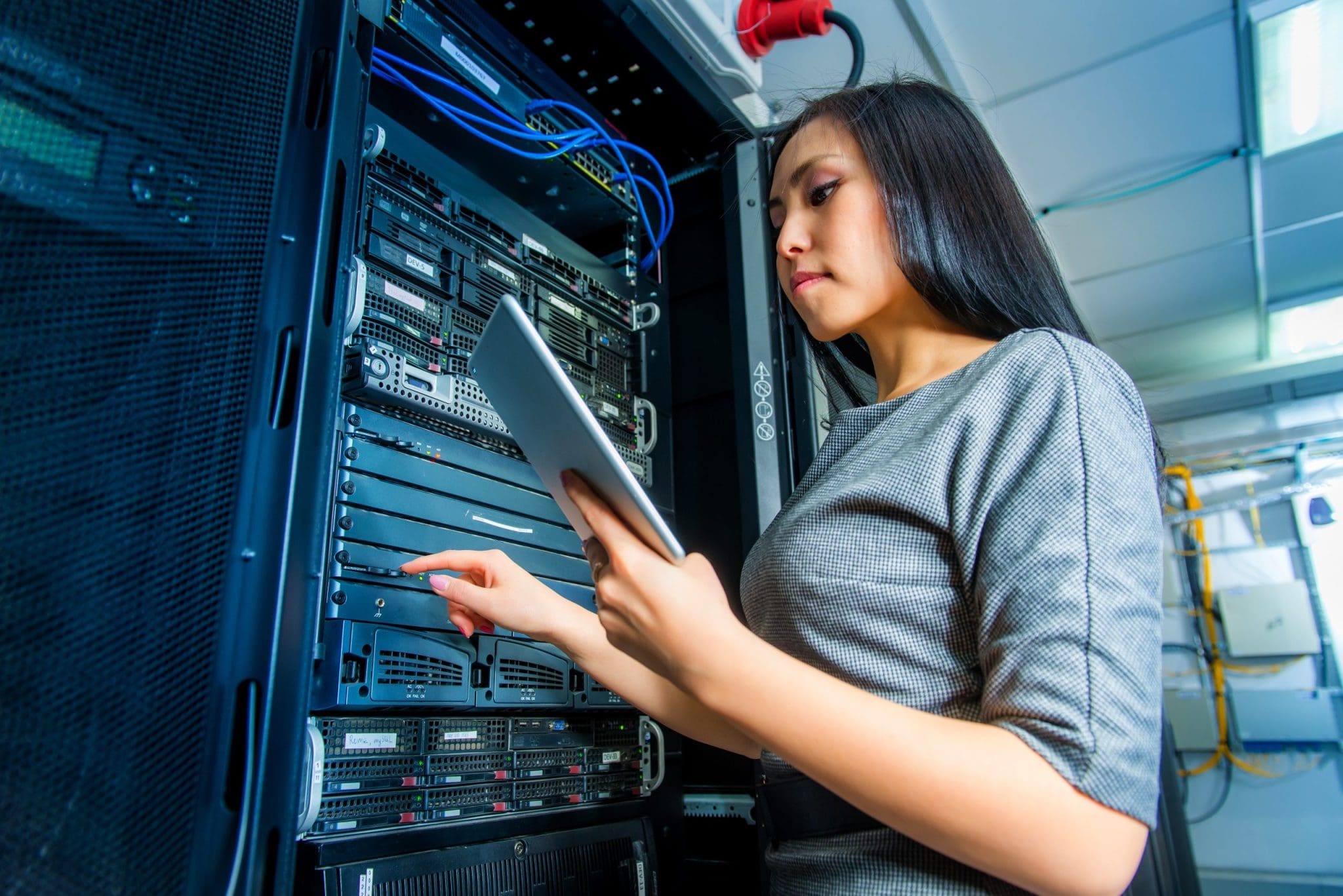Woman working in a data centre with a tablet, managing server equipment