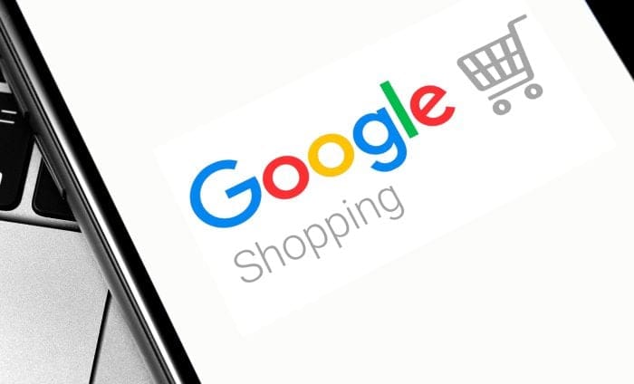 Google Shopping logo displayed on a smartphone screen next to a laptop keyboard
