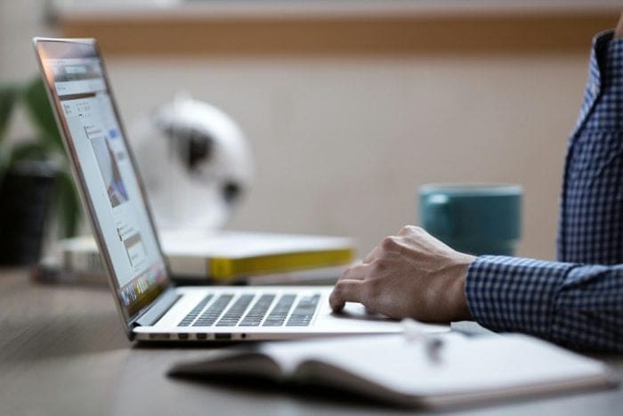 Entrepreneur reviewing project plans on a laptop and notebook, demonstrating the careful balance of quality, speed, and cost in website management.
