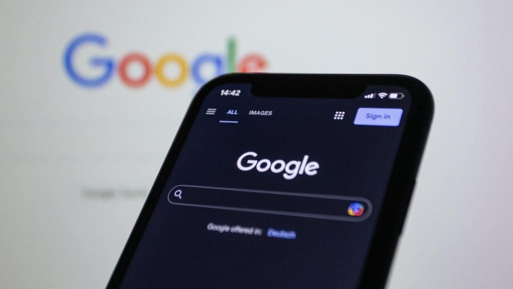 Google on a screen behind a smartphone also displaying the Google search screen