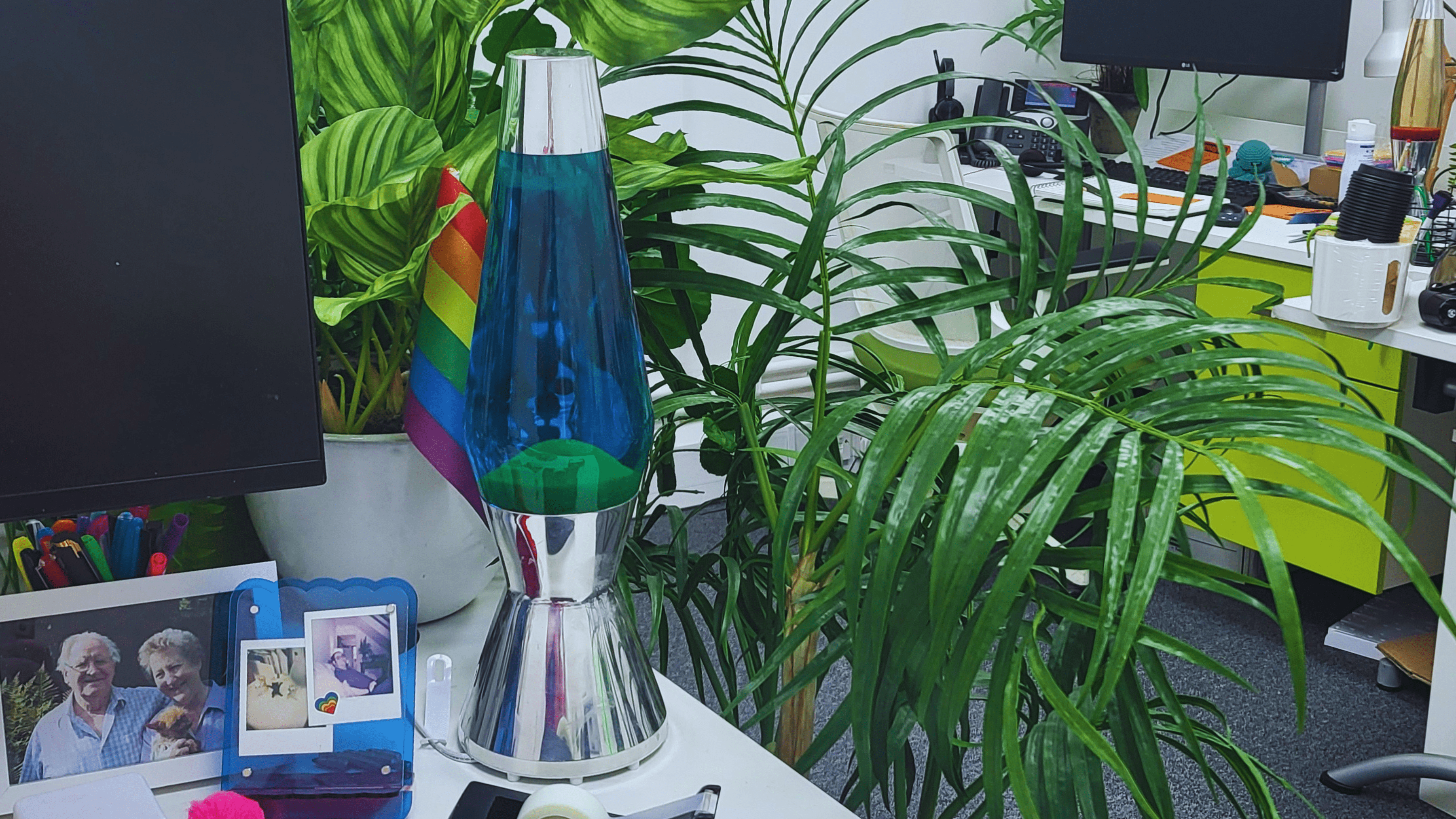 Blue and green lava lamp on desk in O'Brien Media office surrounded by plants and a pride flag
