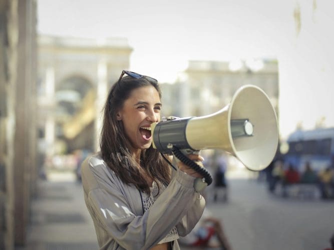 Woman shouting into a megaphone in a sunny street to promote summer website optimisation
